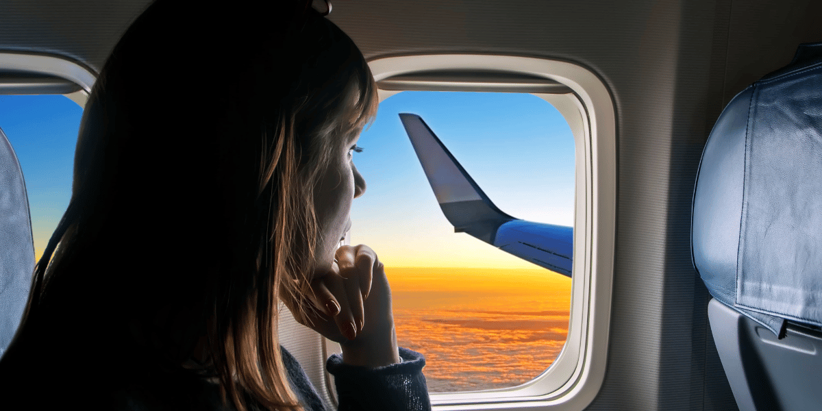 A young beautiful girl looks out the window of the plane to the fantastic clouds at sunset. The passenger looks out the window of the plane to the wing. Travel, vacations, holiday and tourism concept